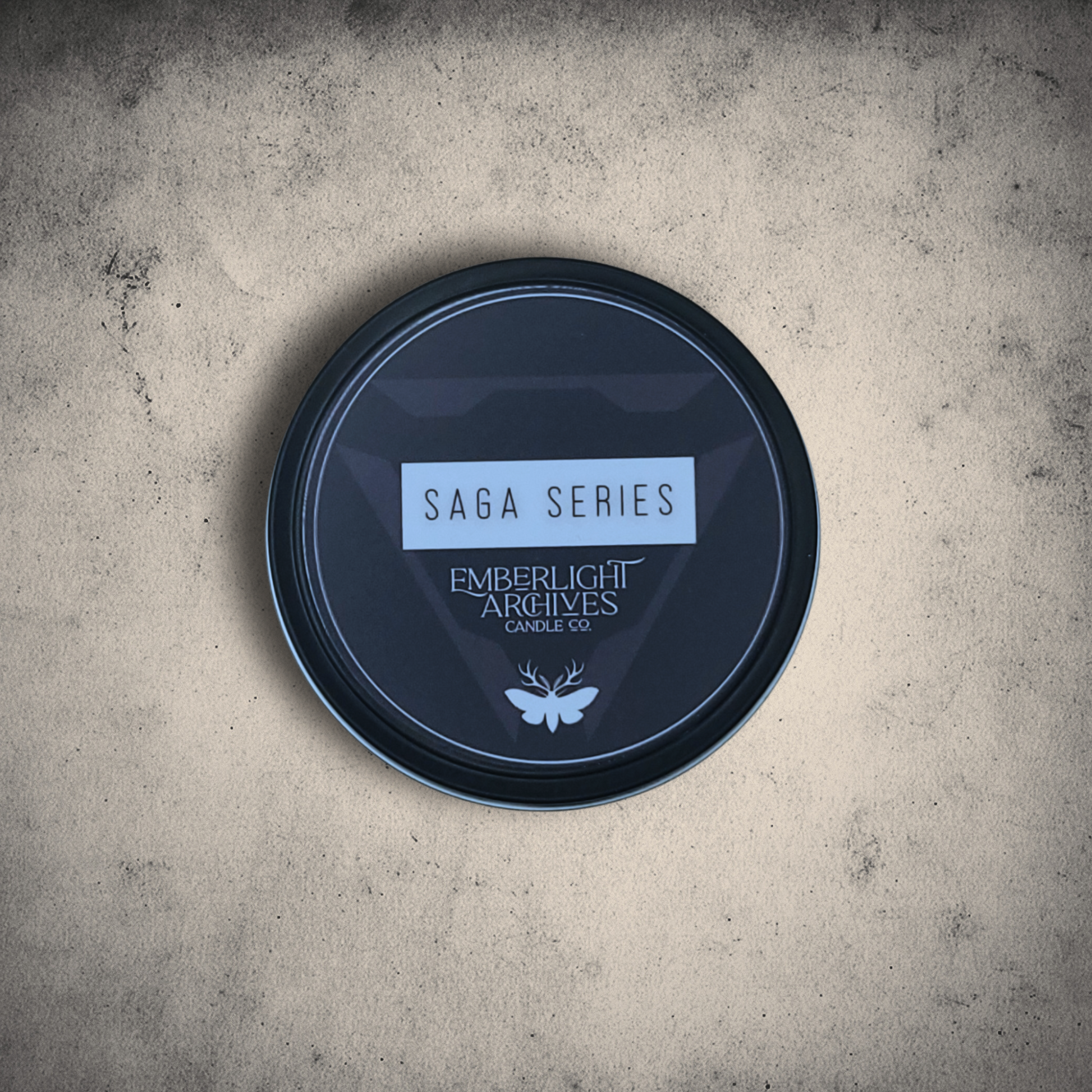Candle lid with 'Saga Series' and 'Emberlight Archives Candle Co.' text on a textured surface