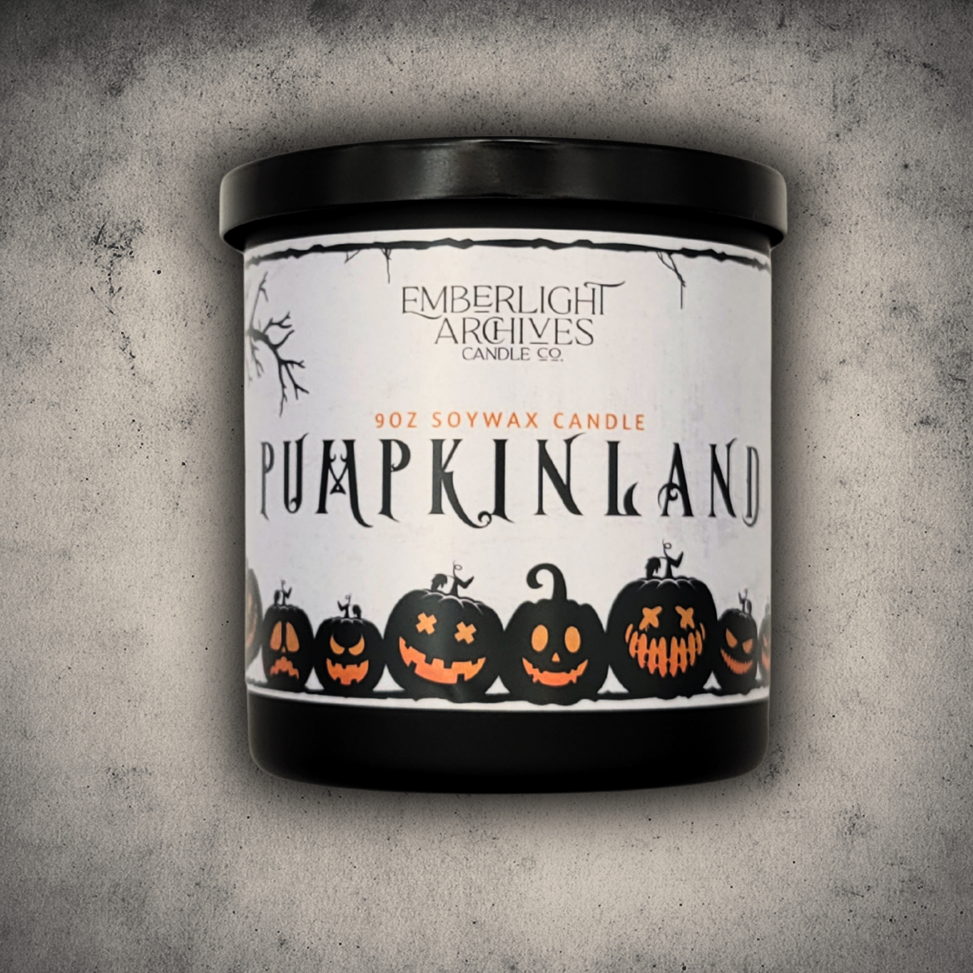 Emberlight Archives Pumpkinland candle in a 9oz black glass jar with whimsical pumpkin label against a gray stone background.