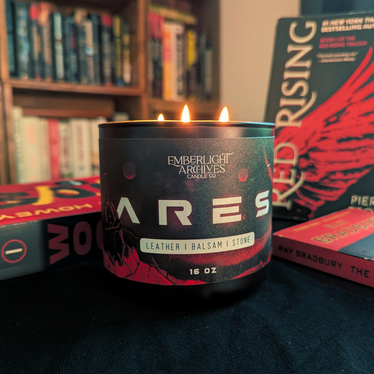 Candle labeled 'Ares' from Emberlight Archives on a surface with books in the background