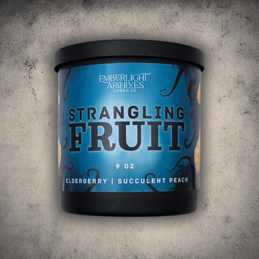 Emberlight Archives Strangling Fruit candle in a 9oz black glass jar with illustrated alien planet label against a gray stone background, Elderberry & Peach scent.