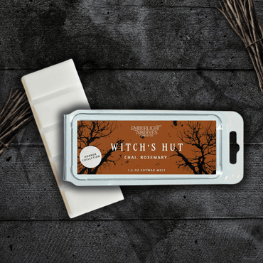Witch's Hut wax melt bar by Emberlight Archives with an orange label against a dark wood background, Chai and Rosemary scent.
