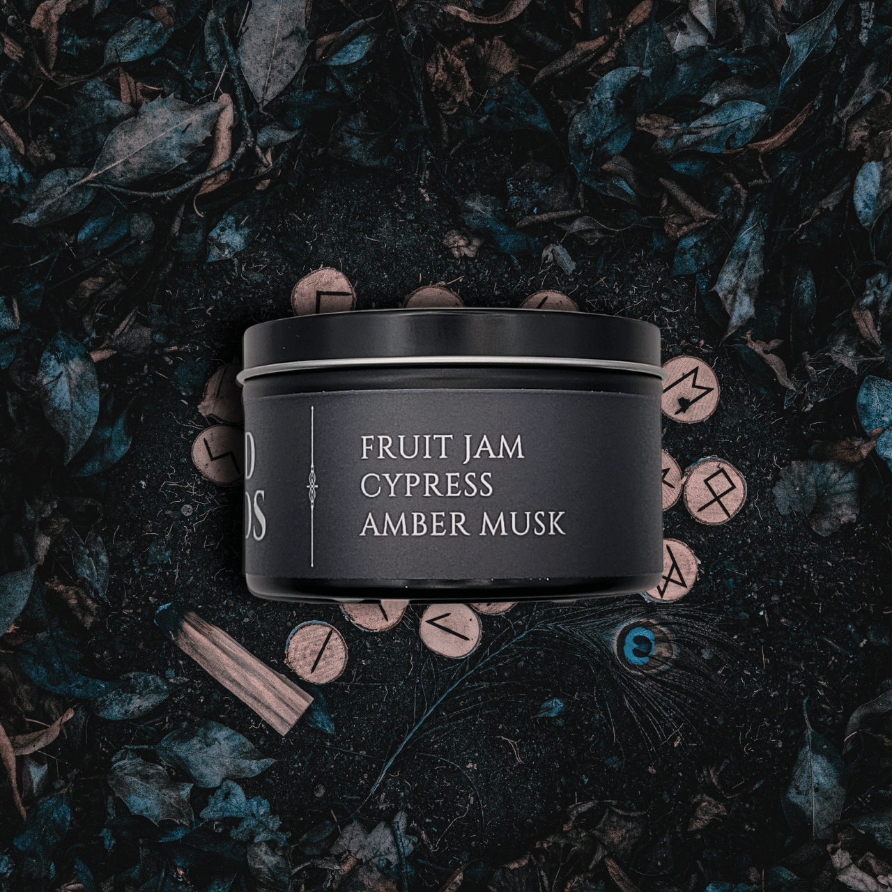 Black candle container with fragrance description reading Fruit Jam, Cypress, Amber Musk on a dark leafy background.