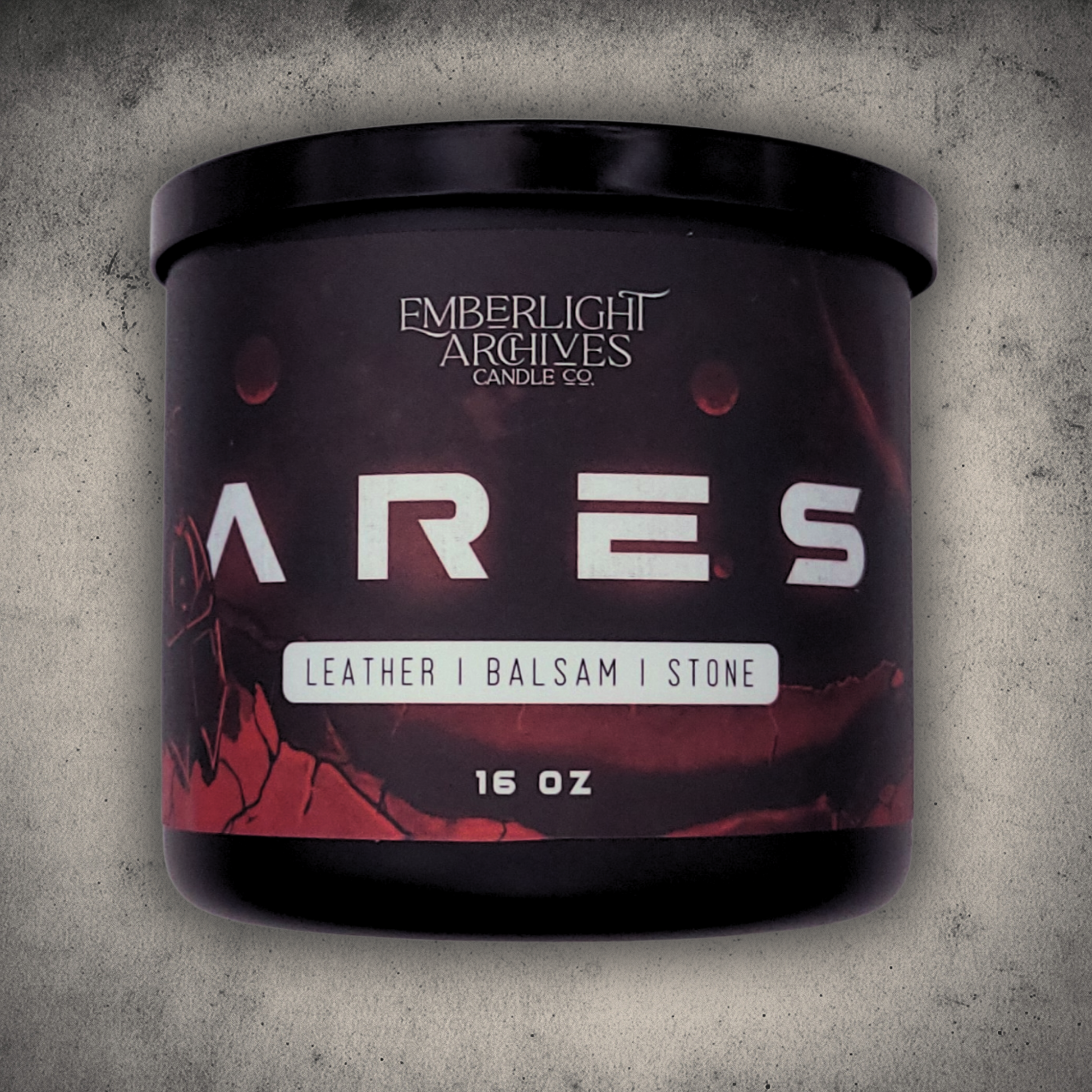 Emberlight Archives Ares candle in a 16oz black glass jar with illustrated red planet label against a gray stone background, Leather & Balsam scent.