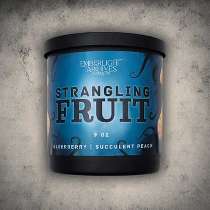 Emberlight Archives Strangling Fruit candle in a 9oz black glass jar with illustrated alien planet label against a gray stone background, Elderberry & Peach scent.