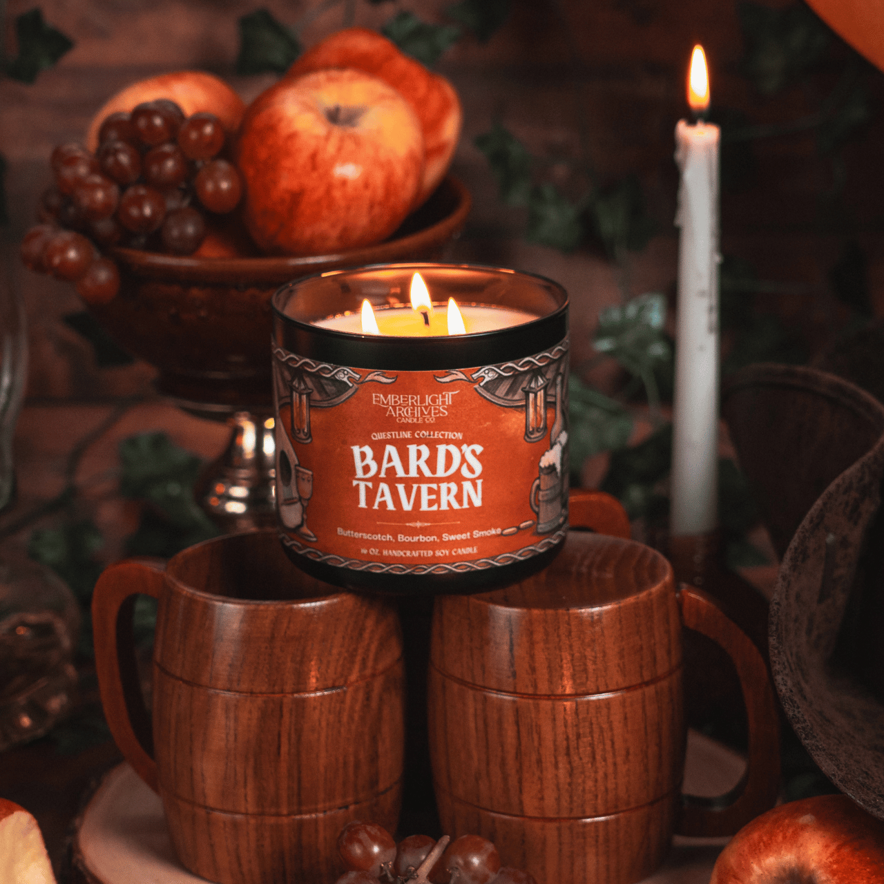 Candle labeled 'Bards Tavern' with wooden mugs and fruit in the background