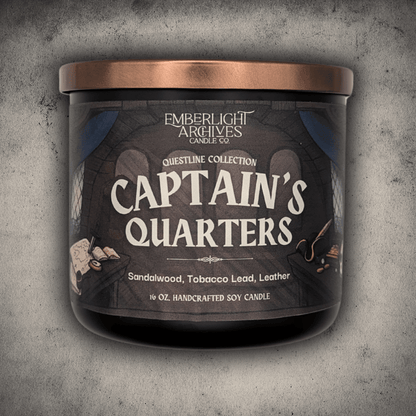 Emberlight Archives Captain's Quarters candle in a 16oz black glass jar with illustrated pirate ship label against a gray stone background, Tobacco and Sandalwood scent.