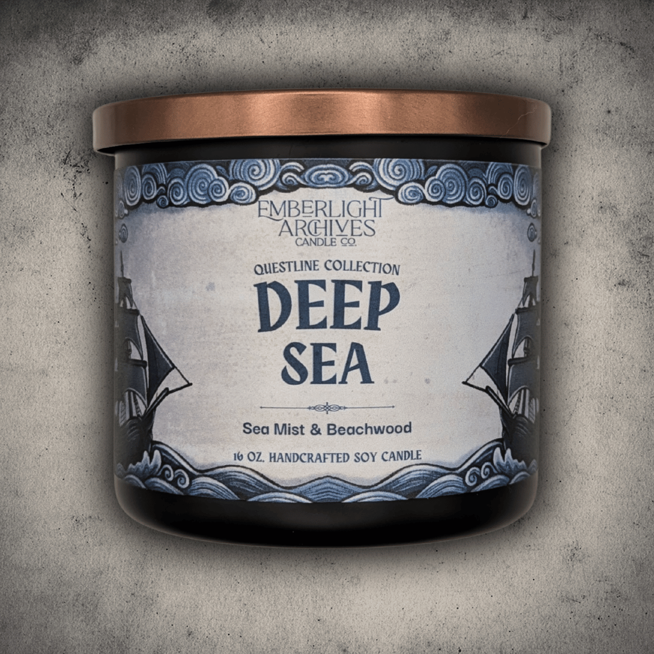 Emberlight Archives Deep Sea candle in a 16oz black glass jar with illustrated sailing ship label against a gray stone background, Sea Mist and Beachwood scent.