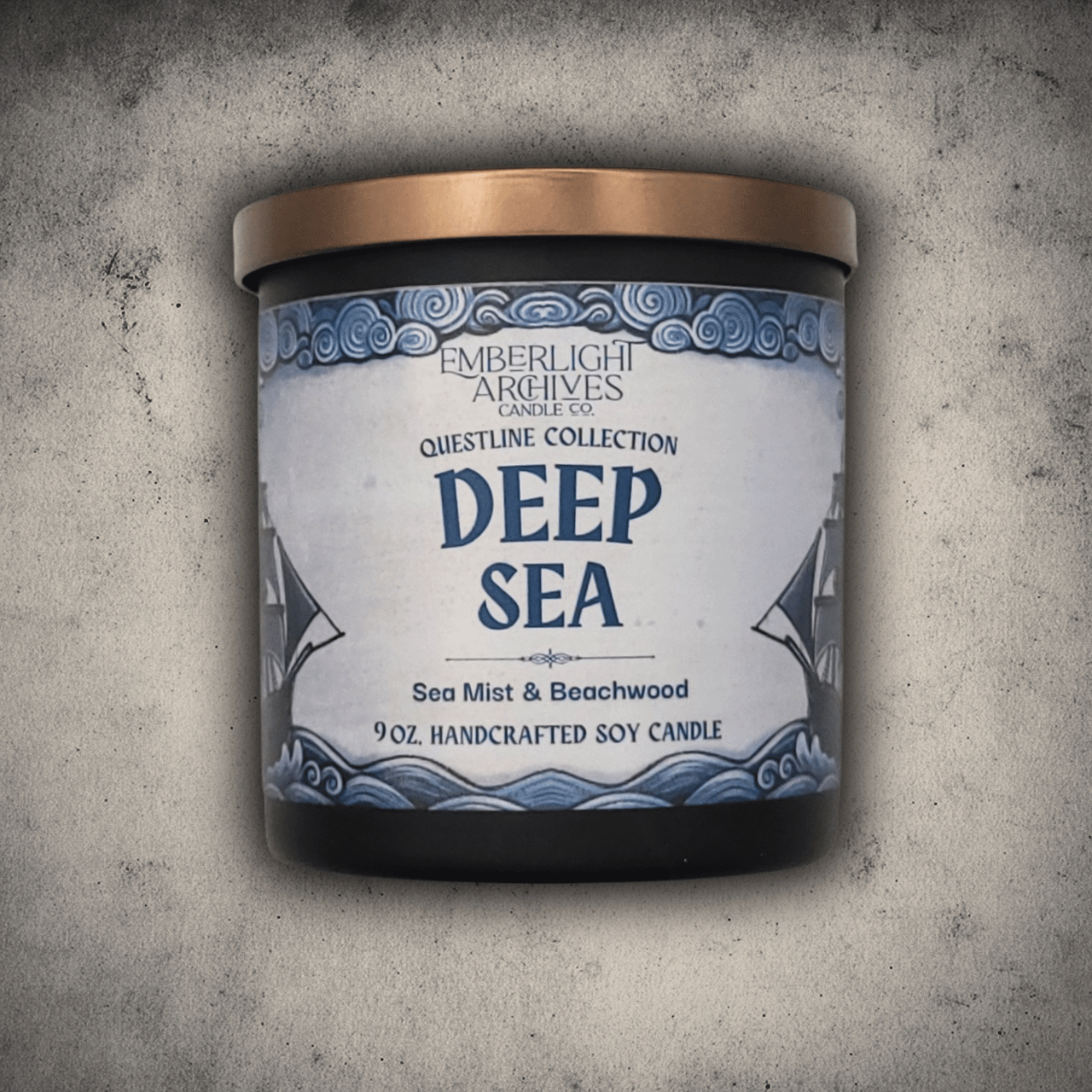 Emberlight Archives Deep Sea candle in a 9oz black glass jar with illustrated sailing ship label against a gray stone background, Sea Mist and Beachwood scent.