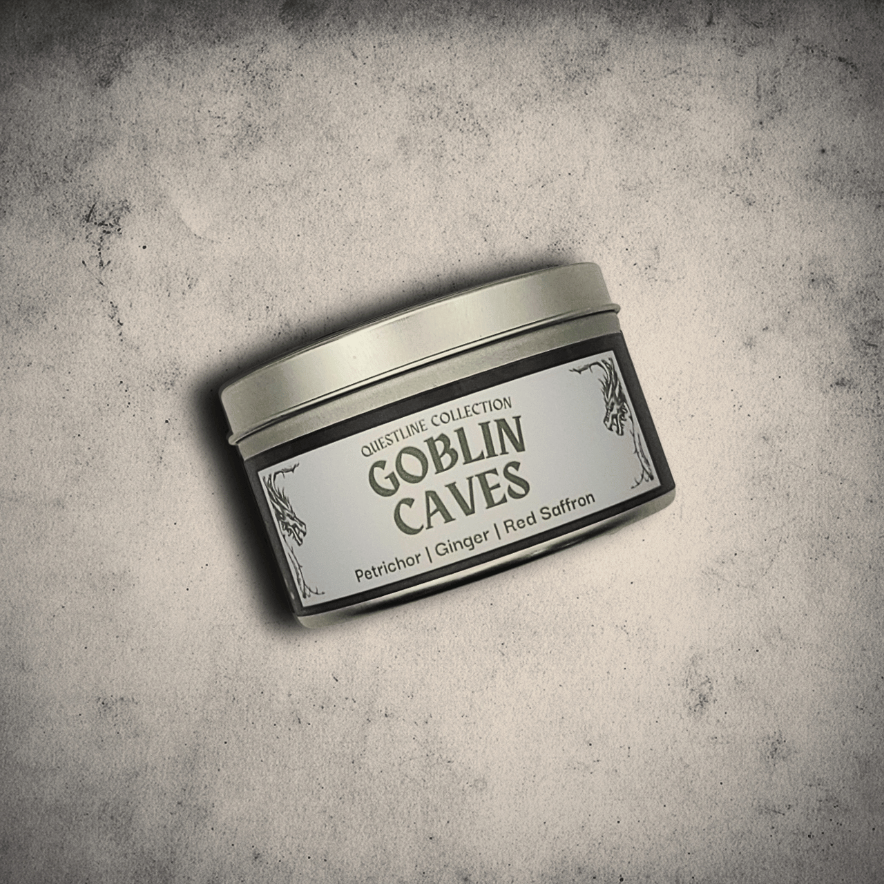 Emberlight Archives Goblin Caves candle in an 8oz black tin with illustrated cave label against a gray stone background, Petrichor and Ginger scent.