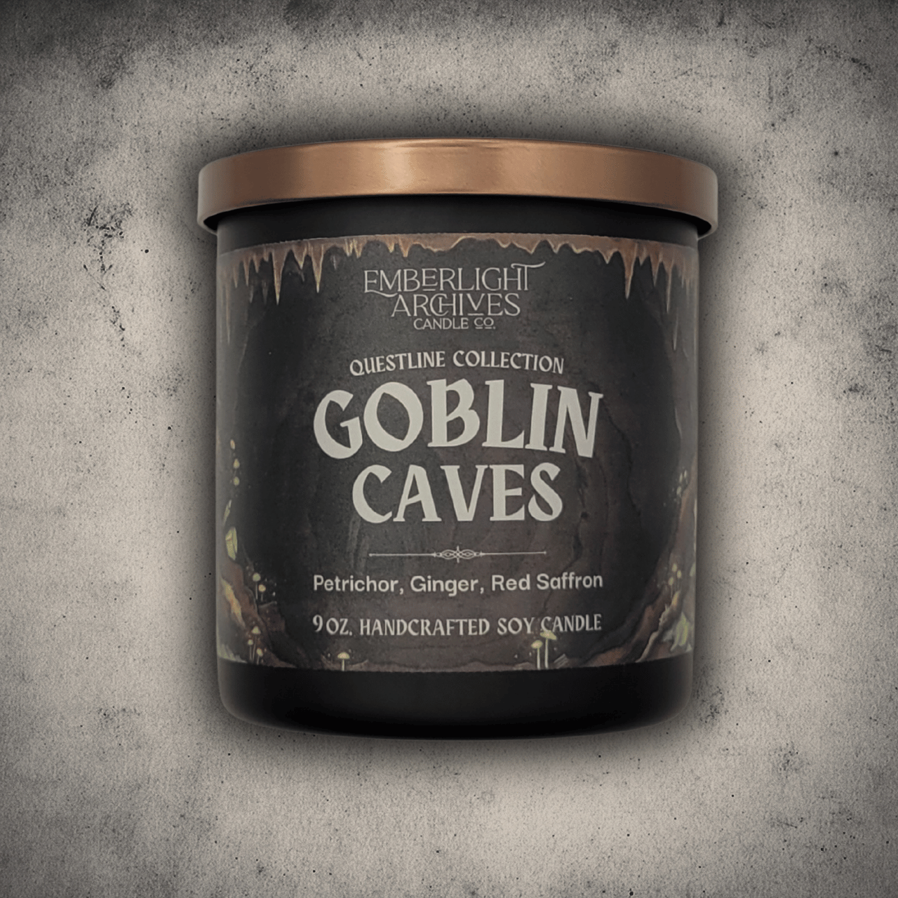 Emberlight Archives Goblin Caves candle in a 9oz black glass jar with illustrated cave label against a gray stone background, Petrichor and Ginger scent.