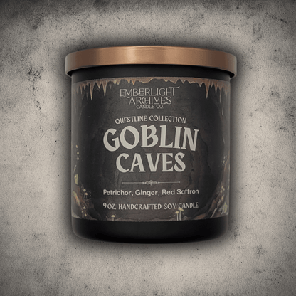 Emberlight Archives Goblin Caves candle in a 9oz black glass jar with illustrated cave label against a gray stone background, Petrichor and Ginger scent.