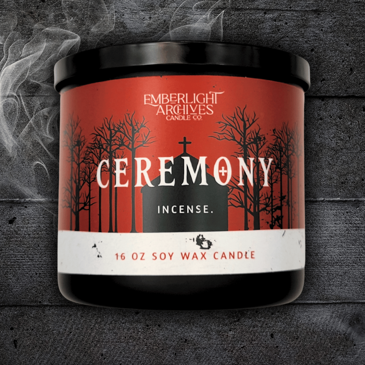 16oz Ceremony candle by Emberlight Archives in a black glass jar with red church scene label against a dark wood background, Incense scent.