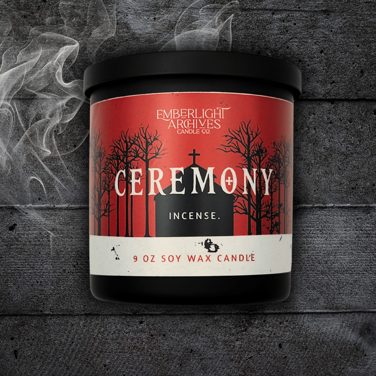 9oz Ceremony candle by Emberlight Archives in a black glass jar with red church scene label against a dark wood background, Incense scent.