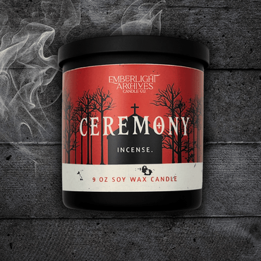 9oz Ceremony candle by Emberlight Archives in a black glass jar with red church scene label against a dark wood background, Incense scent.