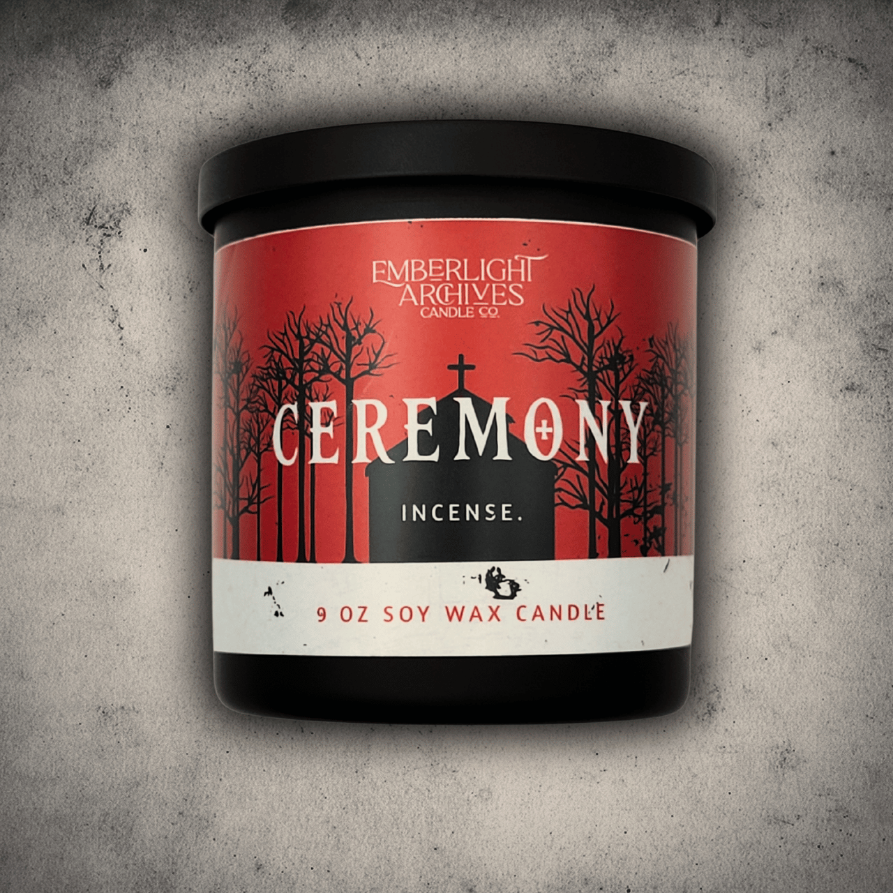 Emberlight Archives Ceremony candle in a 9oz black glass jar with red church scene label against a gray stone background, Incense scent.