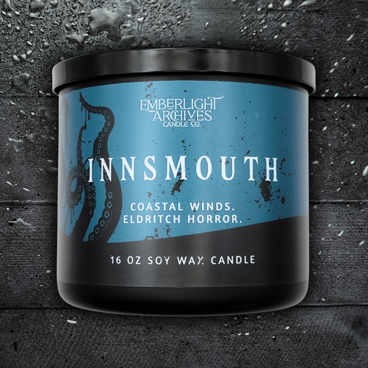 16oz Innsmouth candle by Emberlight Archives in a black glass jar with blue tentacles label against a dark wood background, Coastal Winds and Black Coral scent.