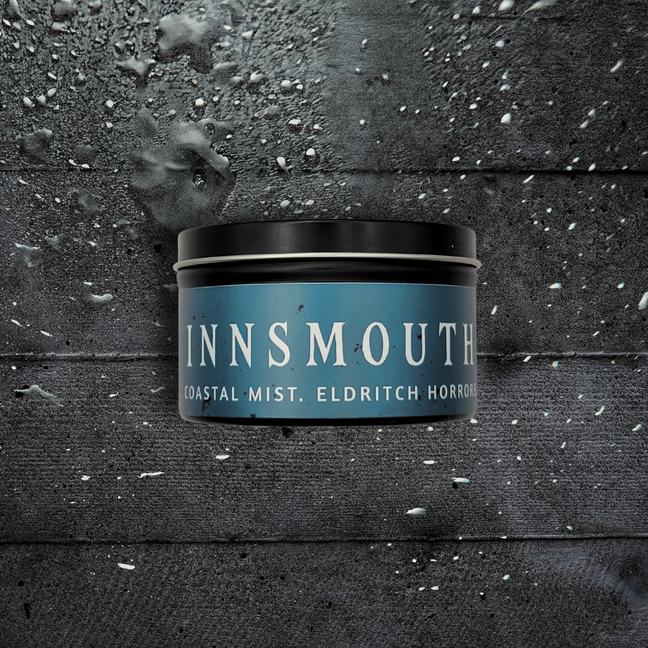8oz Innsmouth candle by Emberlight Archives in a black tin with blue label against a dark wood background, Coastal Winds and Black Coral scent.