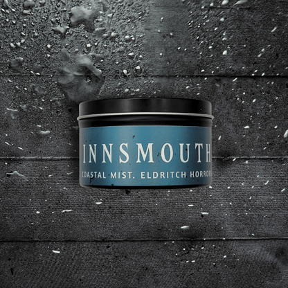 8oz Innsmouth candle by Emberlight Archives in a black tin with blue label against a dark wood background, Coastal Winds and Black Coral scent.