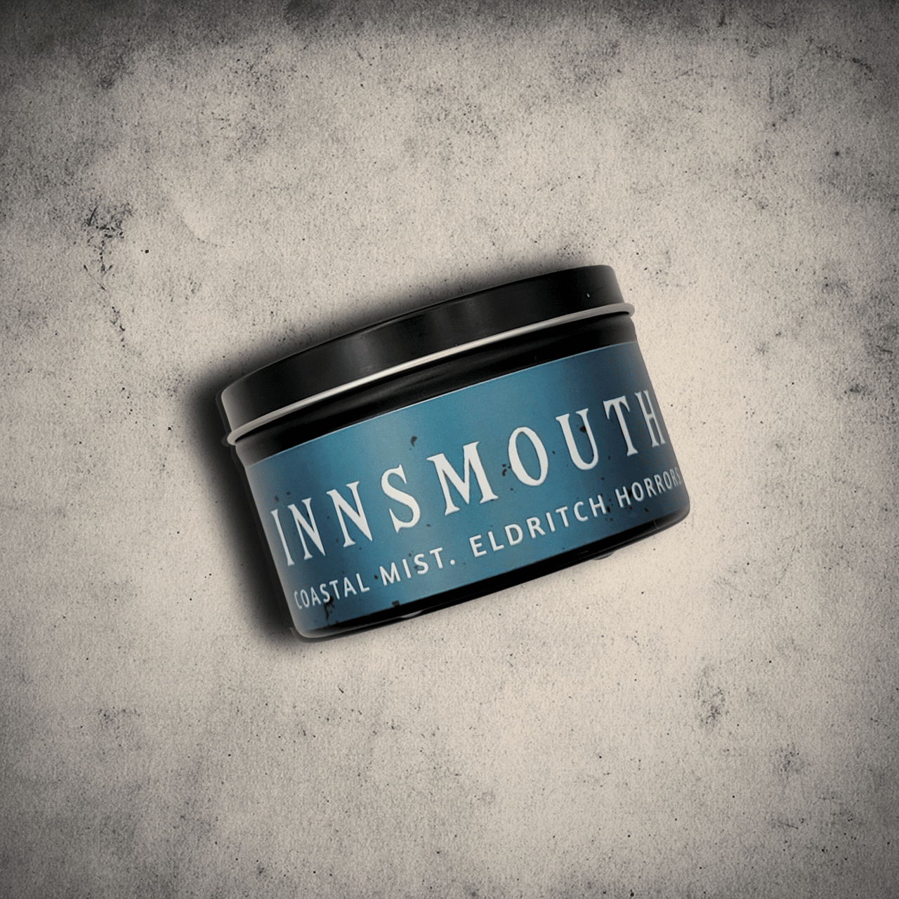 Emberlight Archives Innsmouth candle in an 8oz black tin with blue label against a gray stone background, Coastal Winds and Black Coral scent.