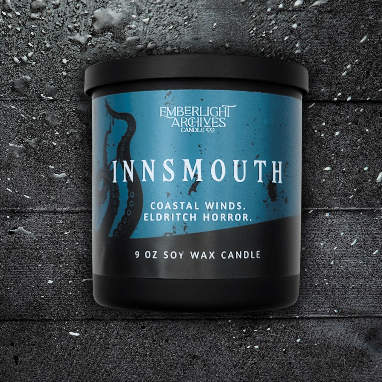 9oz Innsmouth candle by Emberlight Archives in a black glass jar with blue tentacles label against a dark wood background, Coastal Winds and Black Coral scent.