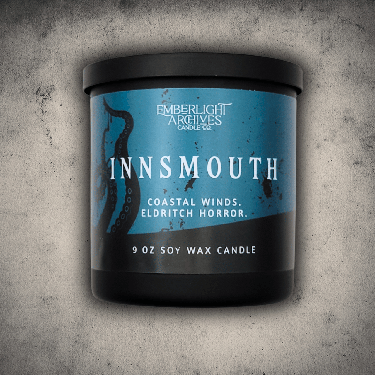 Emberlight Archives Innsmouth candle in a 9oz black glass jar with blue tentacles label against a gray stone background, Coastal Winds and Black Coral scent.