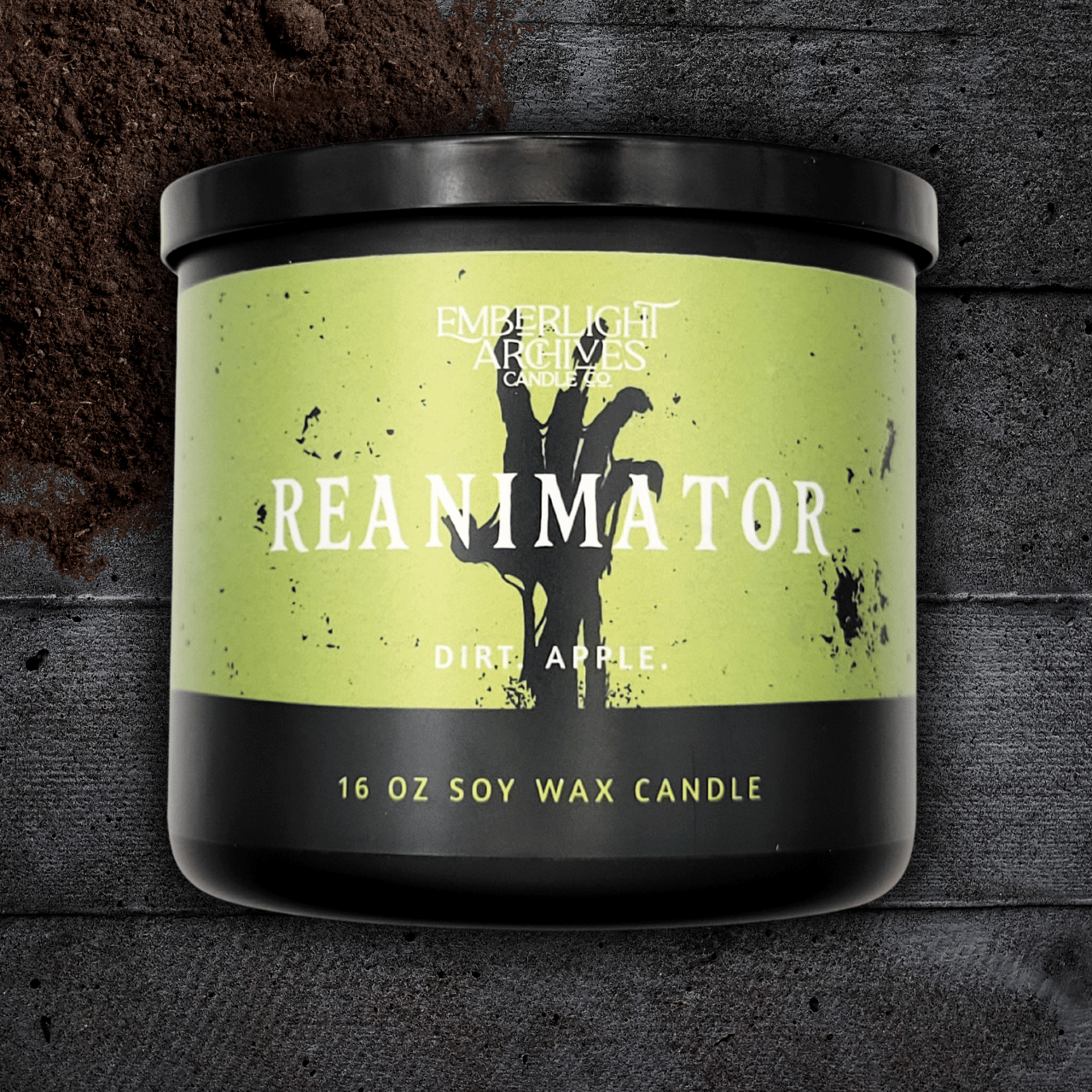 16oz Reanimator candle by Emberlight Archives in a black glass jar with bright green skeleton label against a dark wood background, Dirt and Apple scent.