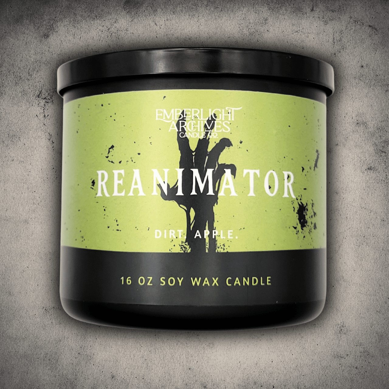 Emberlight Archives Reanimator candle in a 16oz black glass jar with bright green skeleton label against a gray stone background, Dirt and Apple scent.