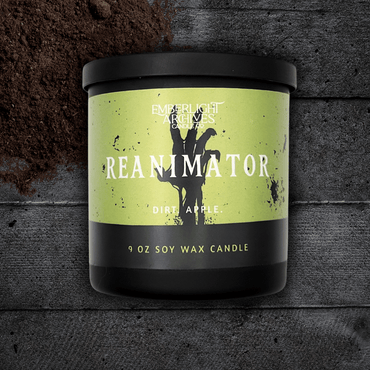 9oz Reanimator candle by Emberlight Archives in a black glass jar with bright green skeleton label against a dark wood background, Dirt and Apple scent.