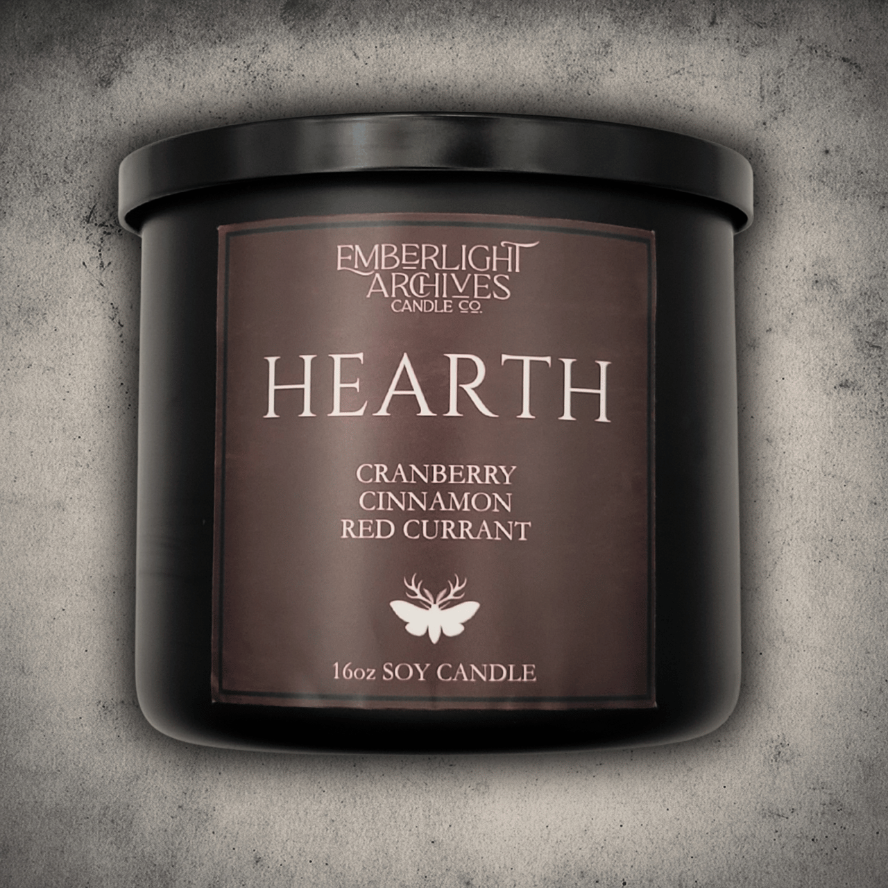 Emberlight Archives Hearth candle in a 16oz black glass jar with red label against a gray stone background, Cranberry Cinnamon scent.
