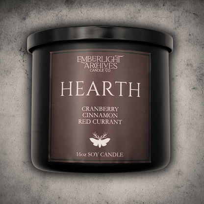 Emberlight Archives Hearth candle in a 16oz black glass jar with red label against a gray stone background, Cranberry Cinnamon scent.