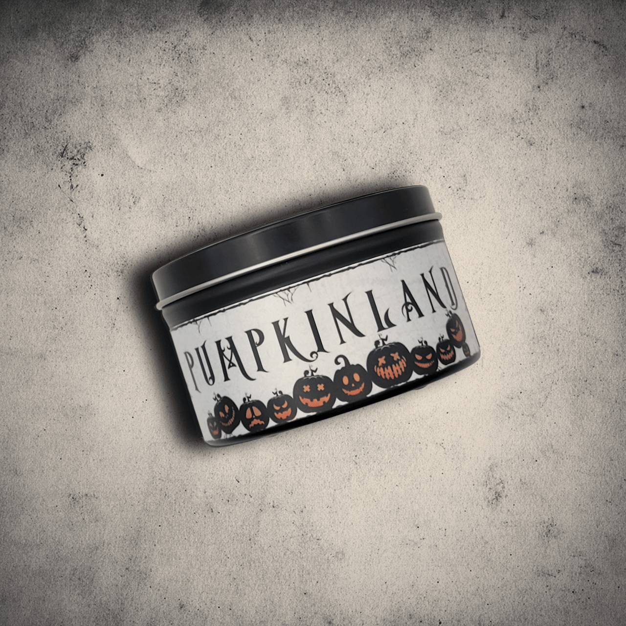Candle tin labeled 'Pumpkinland' with pumpkin design on a textured gray background
