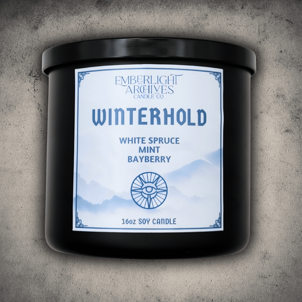 Emberlight Archives Winterhold candle in a 16oz black glass jar with white label against a gray stone background, Spruce, Mint, and Bayberry scent.
