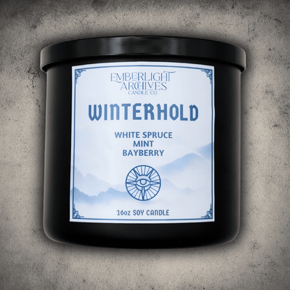 Emberlight Archives Winterhold candle in a 16oz black glass jar with white label against a gray stone background, Spruce, Mint, and Bayberry scent.