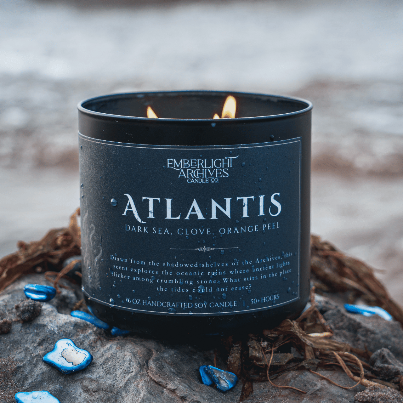 Emberlight Archives Atlantis candle in a 16oz black glass jar with dark label against a outdoor beach background, Dark Sea and Orange Peel scent.