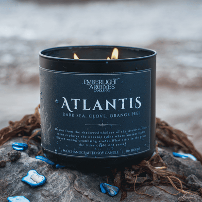 Emberlight Archives Atlantis candle in a 16oz black glass jar with dark label against a outdoor beach background, Dark Sea and Orange Peel scent.