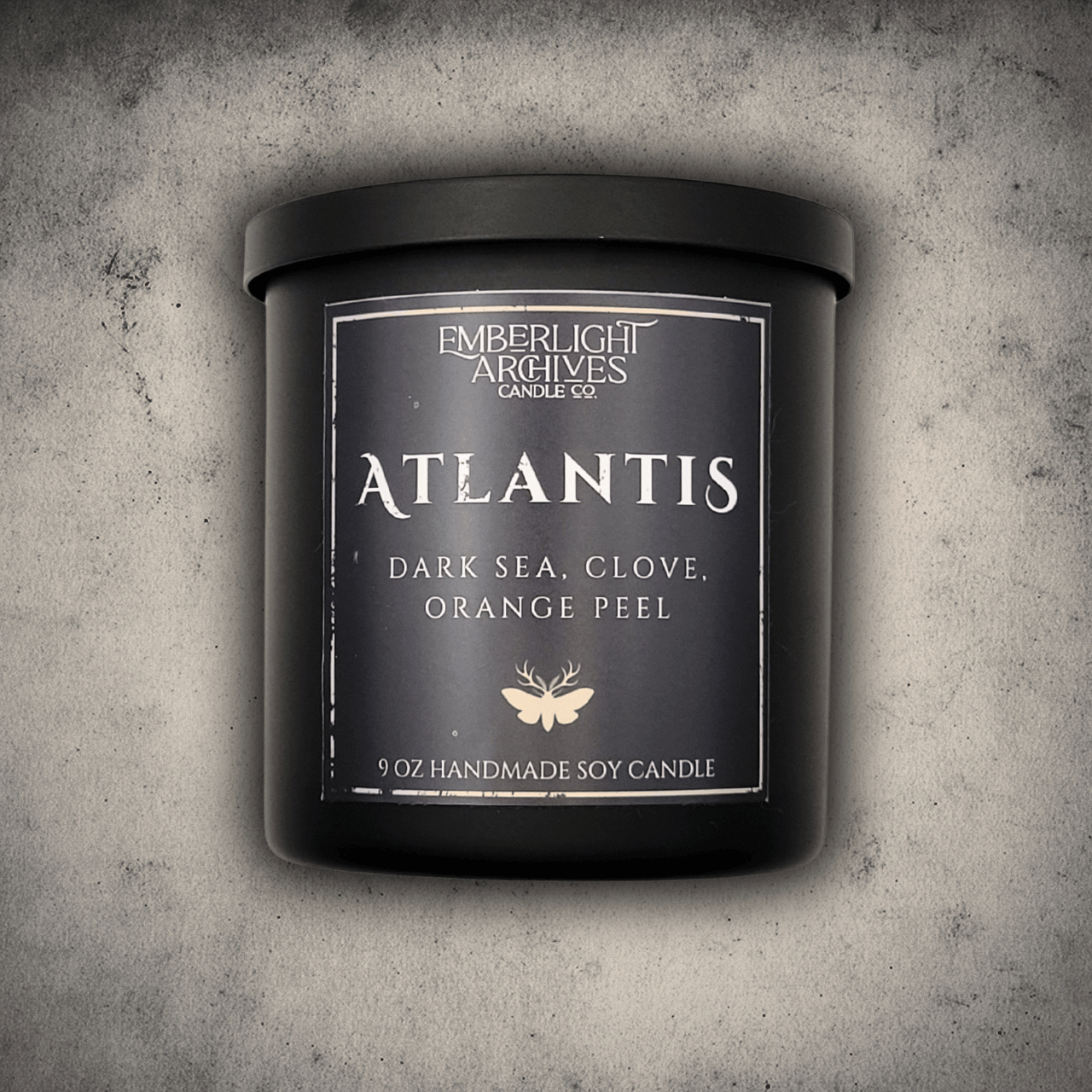 Emberlight Archives Atlantis candle in an 8oz black tin with dark label against a gray stone background, Dark Sea and Orange Peel scent.