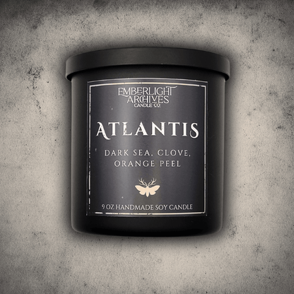 Emberlight Archives Atlantis candle in an 8oz black tin with dark label against a gray stone background, Dark Sea and Orange Peel scent.