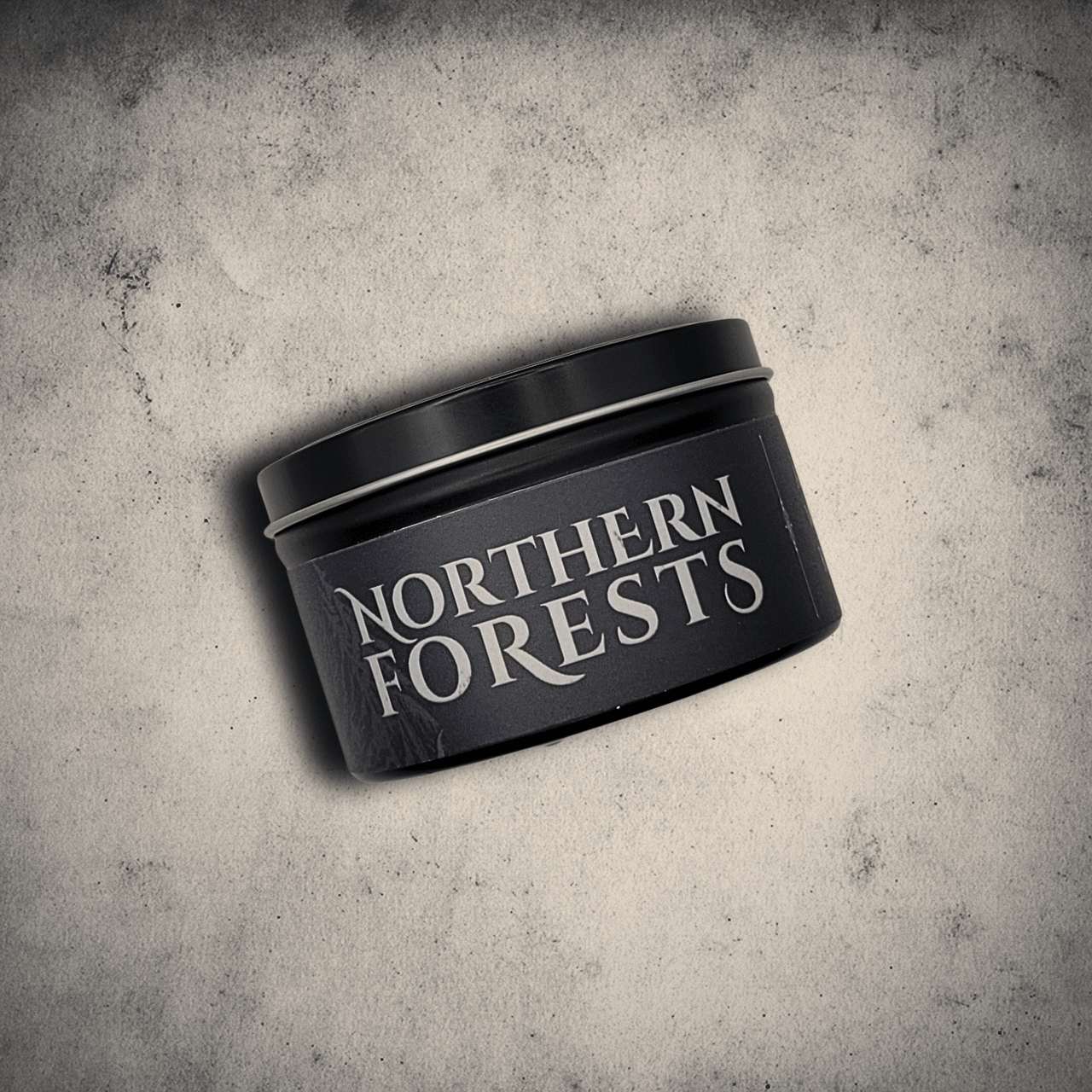 Emberlight Archives Northern Forests candle in an 8oz black tin with dark label against a gray stone background, Rain & Moss scent.