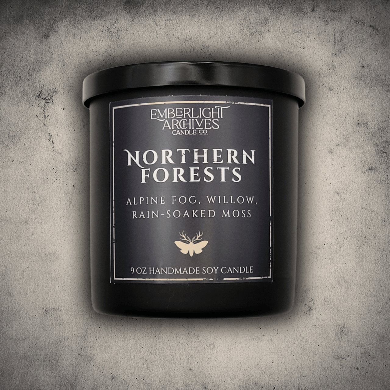 Emberlight Archives Northern Forests candle in a 9oz black glass jar with dark label against a gray stone background, Rain & Moss scent.