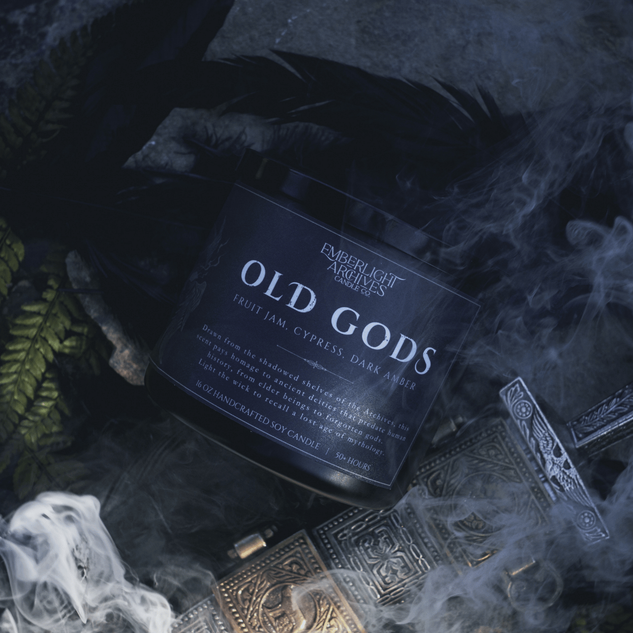 Candle labeled 'Old Gods' from Emberlight Archives on a dark background with smoke, feathers, and a sword.