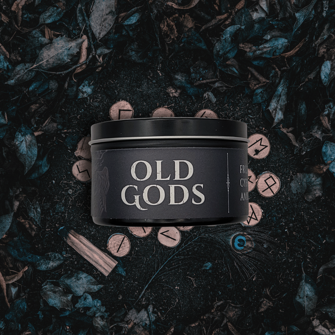 Black 8oz Old Gods candle by Emberlight Archives on a dark background with leaves and symbols.
