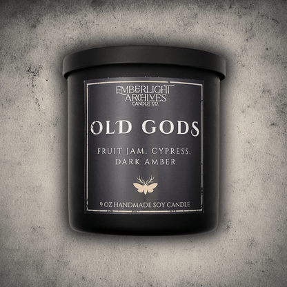 Emberlight Archives Old Gods candle in an 8oz black tin with dark label against a gray stone background, Fruit Jam & Musk scent.